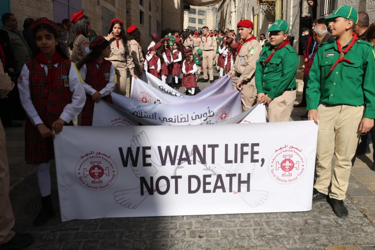 Πρόσκοποι κρατούν μια πινακίδα που γράφει «Θέλουμε ζωή, όχι θάνατο» κατά τη διάρκεια της παραδοσιακής χριστιανικής πομπής προς την εκκλησία της Γέννησης στη Βηθλεέμ (Φωτο: ΑΠΕ-ΜΠΕ/EPA/ALAA BADARNEH)