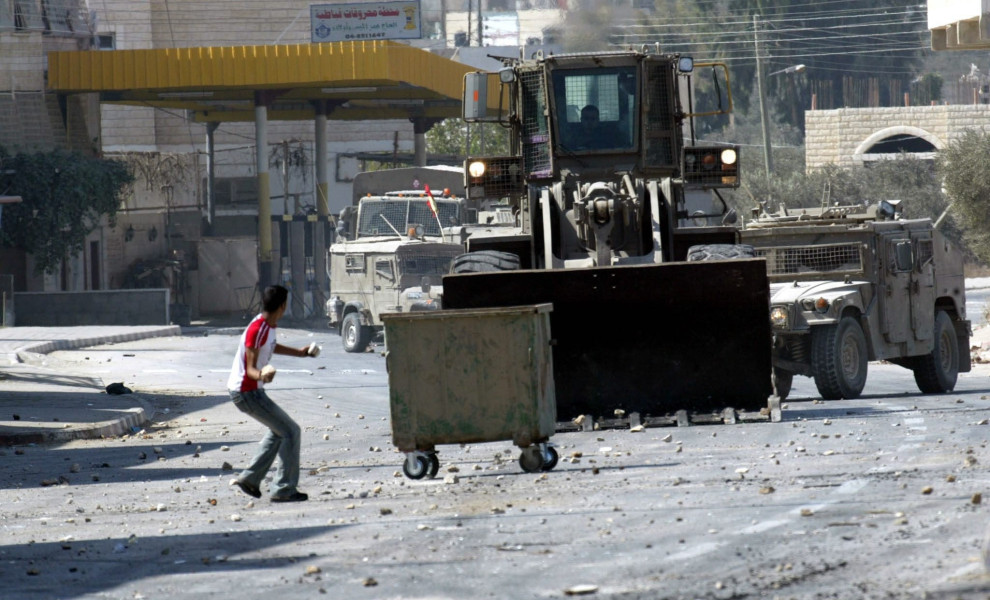 epa000288544 A Palestinian boy hurls stones at an Israeli bulldozer during clashes in Qabatya village, near the West Bank city of Jenin, during an army operation in the village, Tuesday 05 October 2004. Witnesses said that Israeli soldiers took positions 